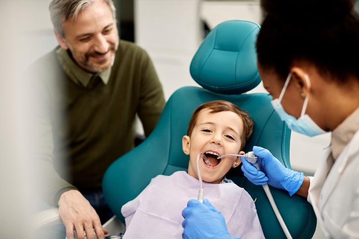 Smiling child sitting in a dental chair during the first checkup at Elite Dental of Highland. 