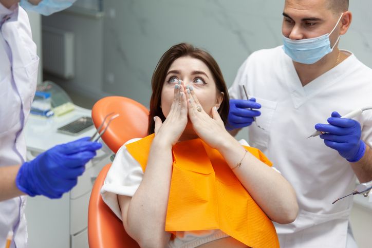 Scared young woman covered her mouth with her hands at the dental clinic. Fear of dentists. Dental treatment concept