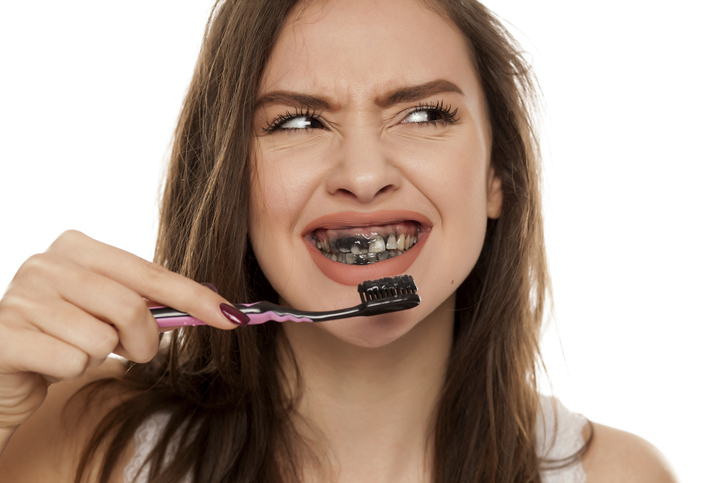 young woman brushing her teeth with a black tooth paste with active charcoal, and black tooth brush on white background